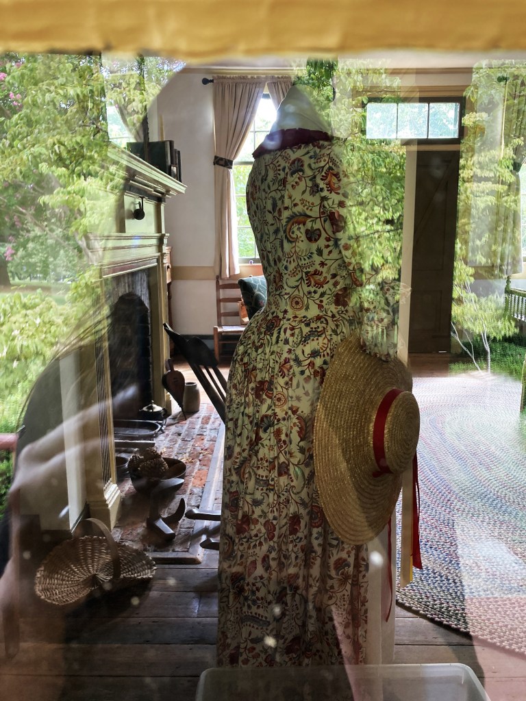 A layered image, looking through the window into the interior of a house built in the 1790s. Image shows interior view, reflection of outside, and silhouette of the photographer.